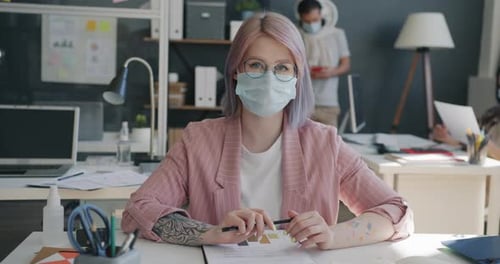 Portrait of Attractive Young Blonde Wearing Medical Mask Sitting at Desk in Office