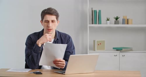 Concentrated Caucasian Millennial Businessman Sitting at Home Desk or in Office Looking at Documents