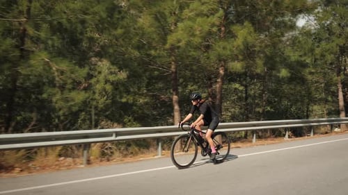 Professional female triathlete in protective cycling helmet and sunglasses cycling on road