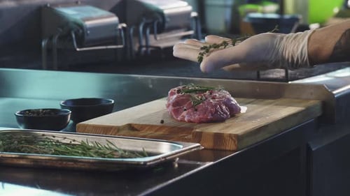 Chef Seasoning Raw Meat with Rosemary and Pepper
