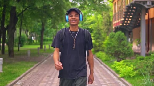 Young Man Smiling Walking With Headphones in Park