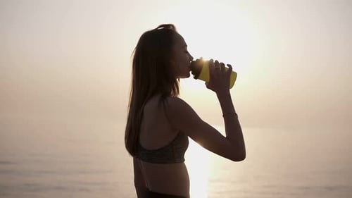 Woman Drinking Water at Sunrise on the Beach