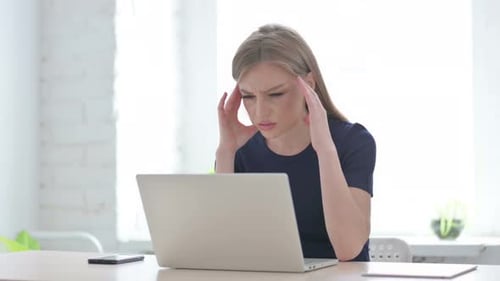 Stressed Young Adult Woman Massaging Temples at Desk