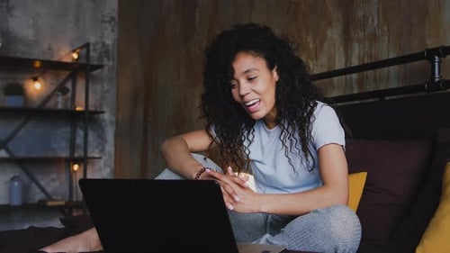Junge attraktive afroamerikanische Frau, die Laptop für einen Videoanruf benutzt, der im Bett Dolly sitzt