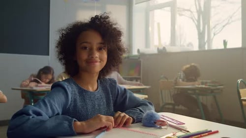 Smiling Schoolgirl Sitting at Desk in Classroom