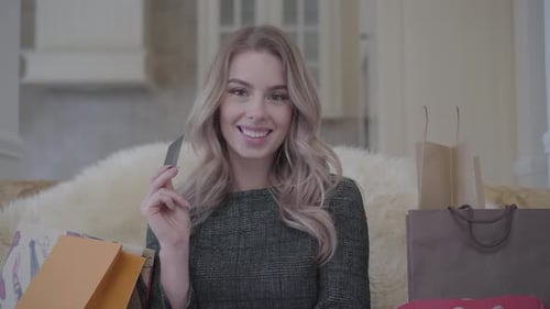 Portrait of a Confident Smiling Pretty Young Woman Sitting on the Sofa with a Lot of Shopping Bags