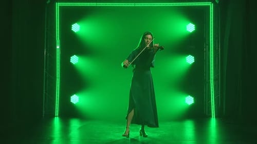 Violinist Woman in a Long Black Dress Plays the Violin. Rehearsal in a Smoky Studio with Green