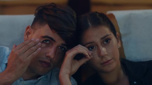 Attractive cheerful young caucasian couple crying while watching film in movie theater