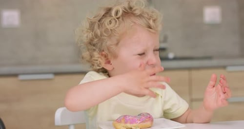 Happy Child Eating a Donut at the Table