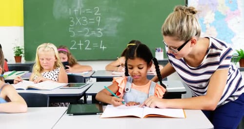 Teacher Helping Student Write in Classroom