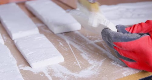 Worker Paints White Plaster Brick Cast at Wooden Table