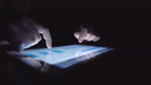 Person Interacting with Bright Tablet in Dark Room