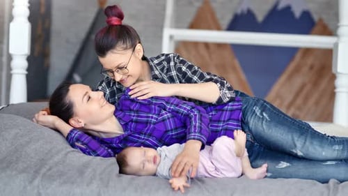 Loving Women Cuddle with Sleeping Baby on Bed