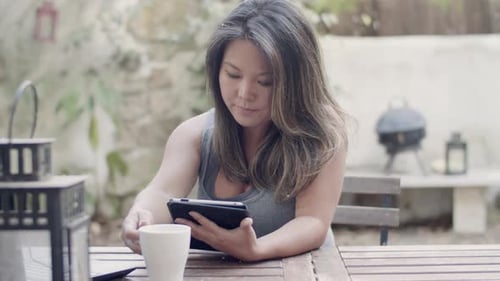 Focused Woman Sitting at Table in Outdoor Cafe with Tablet