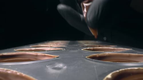 Chocolatier Fills Chocolate Molds with Liquid Chocolate Filling for Praline Sweets , Making of