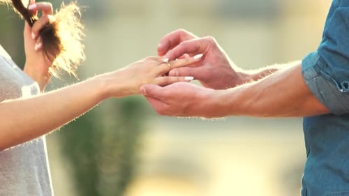 Man Putting Engagement Ring on Woman Hand Outdoors