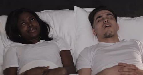 Multi-ethnic Couple Lying in Bed Together. Woman Suffers From Her Partner Snoring in Bed