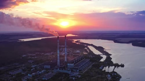 Factory on colorful sky background at sunset. Manufacturing near the river. Aerial view.
