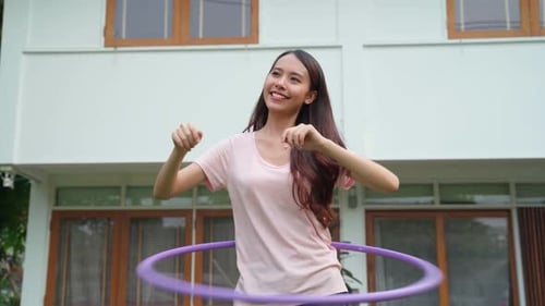 Asian Beautiful young woman doing cardio workout, rotating hula hoop in garden at house.