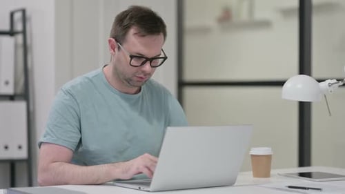 Man Works at Desk on Laptop in Office