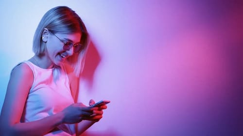 Smiling Woman Using Smartphone in Neon Lit Room