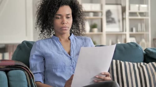 Woman Carefully Reviews Documents at Home on Couch