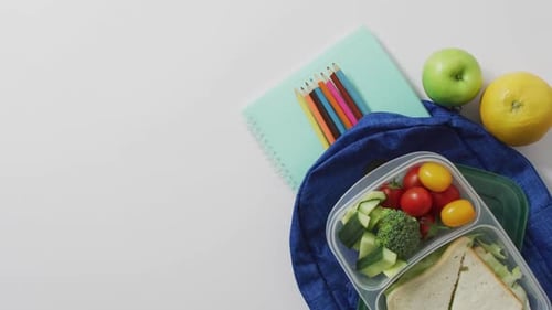 Vídeo de un almuerzo saludable para llevar de frutas y verduras, con lápices de colores en la mochila escolar