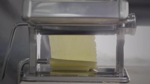 Pasta Dough Being Rolled Through Pasta Machine