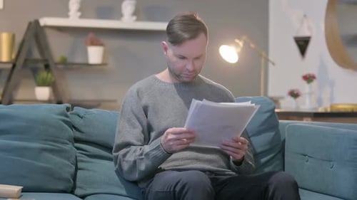 Man Sitting Indoors Reading Documents on Couch