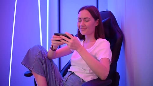 Mujer joven sonriente jugando al juego de Aplicación teléfonos móviles. Joven mujer caucásica disfrutando del Vídeo de un teléfono