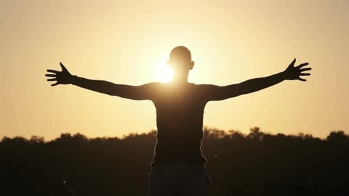 Silhouette of Young Man Raising Hands To Sides and Up Against Sunset Slow Motion