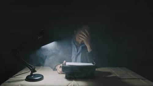 Man Typing at Typewriter Under Lamp in the Dark