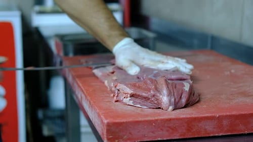 Butcher Slicing Raw Red Meat with Sharp Knife