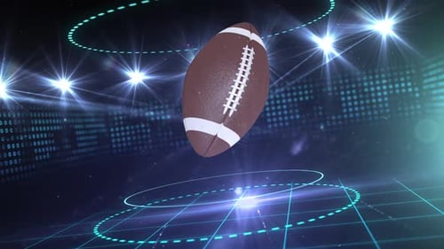 Animation of a rugby ball rotating in front of sports arena stadium lit by rows of spotlights on dar