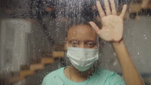 Person in Mask Behind Rain-Streaked Glass