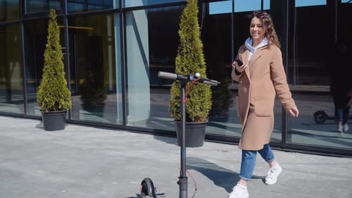Woman Looking at Smartphone Next to Electric Scooter