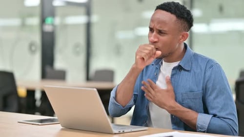 Sick Casual African Man with Laptop Coughing in Office