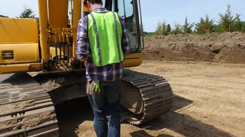 Man Inspecting Excavator on Construction Site on Sunny Day
