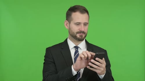 Cheerful Businessman Scrolling His Cellphone Against Chroma Key