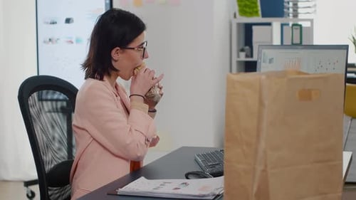 Geschäftsfrau isst einen Bissen leckeres Sandwich und trinkt Kaffee vor dem Monitor