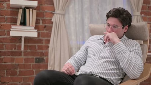 Distressed Man in Rocking Chair Rubs Eyes