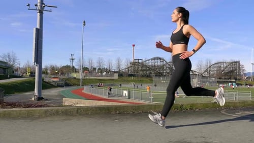 Woman Running on Pavement Near Track on Sunny Day