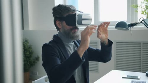 Grey-haired Man in Suit Enjoying Virtual Reality Glasses Moving Arms at Desk in Office