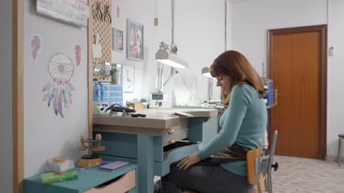 Young Freelance Jeweler With Apron Working On Table At Her Workshop