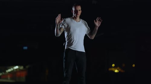 Man Stands at Night With Hands Up