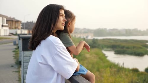 Careful Mother Holds Hand of Little Girl on City Embankment