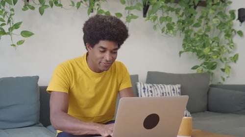 Young Adult Smiling While Typing on Laptop Indoors