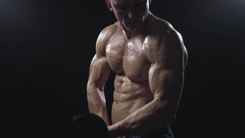 Muscular Man Lifting Dumbbell in Dark Studio