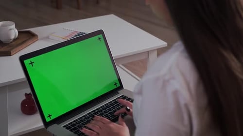 Home Isolated. Woman at Home Sitting on a Couch Works on a Laptop Computer with Green Mock-up Screen