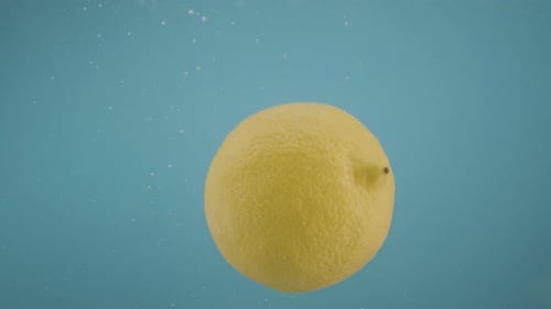 Lemon Falls into Water with Rising Bubbles